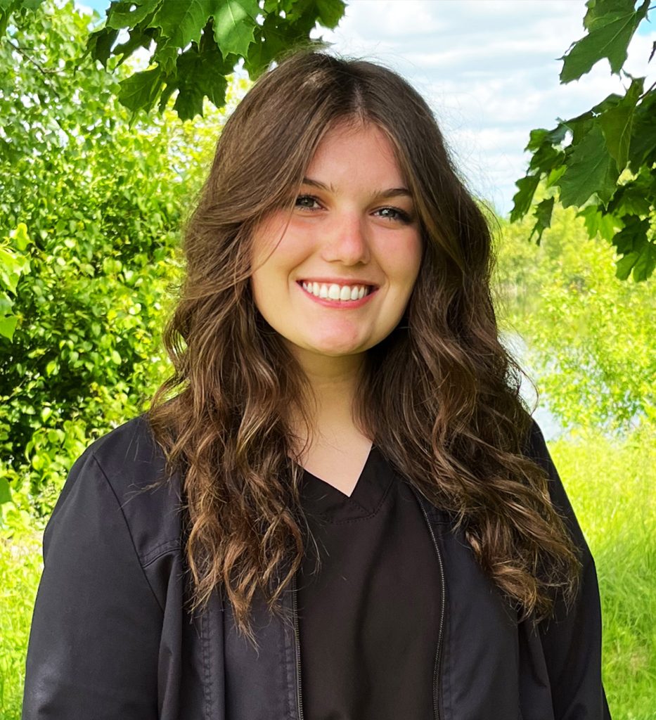 Madeline, dental assistant, smiling outdoors among trees